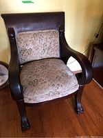 Front angled view showing the full chair with mahogany wood, carved arms, and cushioned floral upholstery.