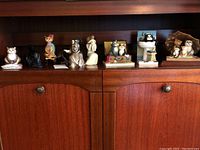 Shelf display with nine figurines including four cat figurines in various poses and scenarios, black soapstone horse figurine, Willow Tree grandmother figurine, and other animal figures