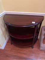Front view of 3-tier demi-lune table showing semi-circular shape, wood finish, and scratches on top surface.