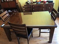 Full view of wooden dining table with glass top and four ladderback chairs in a room.