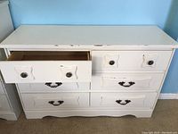 Front view of white painted dresser with six drawers, top drawers have round metal knobs, lower drawers have drop-style metal handles. One drawer partially open showing wood inside.