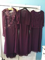 Front view of three burgundy formal dresses with distinct styles hanging on hangers.