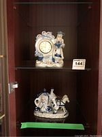 Shelf display showing both blue and white porcelain figurines, clock on upper shelf and horse figurine below