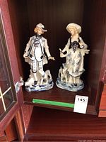 Figurines displayed inside a glass cabinet, showing both man and woman with dogs, 12.5 inches tall, blue and white porcelain