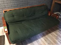 Full view of wooden framed futon with green mattress cover in a room with dark wall.