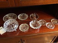Full set of assorted crystal and glassware items displayed on wooden surface including candy dish, pickle dish, juicer, and coasters.