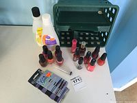 Image showing multiple nail polish bottles in various colors, nail polish remover bottles, and a pack of bobby pins on a white surface with a green basket background.