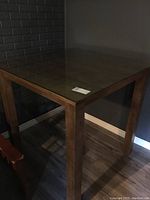Full view of the square pub height wooden table with glass cover, showing table legs and corner.