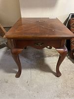 Front view of wooden side table showing Queen Anne style legs and drawer with metal pull handle, visible scratches on surface.