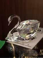 Photo showcasing clear Swarovski crystal swan figurine on a reflective surface, highlighting prism-like reflections and smooth neck detail.