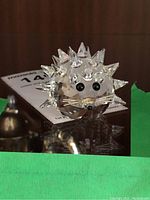 Front angle showing clear faceted crystal porcupine figure with black eyes and nose, sitting on glass surface.