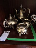 Photo showing full tea service set with visible reflective silver plating and ornate detailing of pots, cream and sugar bowl
