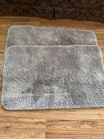Top-down photo showing two grey rectangular plush bathroom mats stacked, highlighting their size and material.