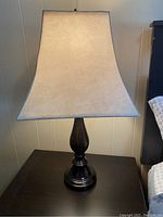 Photo of a 28 inch tall bedroom table lamp showing black turned style base and cream fabric shade with blue trimming.