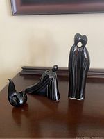 Three black ceramic figurines arranged left to right on a wooden surface in front of a framed picture.