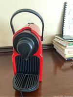 Front view of the red Breville Nespresso coffee maker showing spout and drip tray.