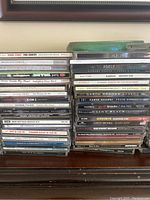 Photo showing stacked CDs with spines visible featuring Adele 25, Alabama Greatest Hits, Garth Brooks albums, Clint Black, Aerosmith Classics Live, Blues Brothers, Harry Connick Jr.