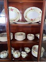 Front view of china pieces arranged in cabinet showing platters, plates, and bowls with floral pattern on yellow background