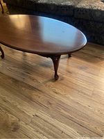 Side view of the mahogany oval coffee table showing the shape and style of cabriole legs on wooden floor.
