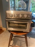 Front view of stainless steel Cuisinart air fryer toaster oven sitting on a wooden stool showing control dials.