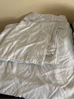 Photo of double bed sheet set with a gray leaf-like pattern on white background, folded on bed