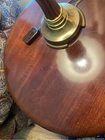 Close-up image of one round mahogany end table showing the surface wear, scratches, and finish around a brass lamp base.