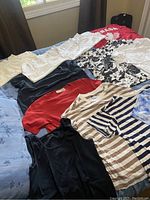 Photo of ladies' t-shirts and tank tops laid out on bed showing variety of colors and patterns including solid colors, stripes, floral, and tie-dye