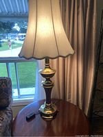 Full view of the 36-inch tall table lamp showing brass and dark wood base, along with the cream-colored shade with scalloped edges.