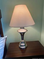 Single table lamp with silver-toned metal base and cream fabric shade on dark brown wooden table.