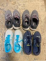 Top view of four pairs of New Balance running shoes arranged in two rows, colors grey/pink, white/blue, and navy blue.