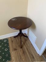 Round wooden occasional table in corner showing overall shape and condition including three legs and central column.