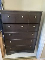 Front view of the tall dark brown wood dresser showing five drawers with round metal knobs.