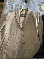 Grey women's blazer size 16 shown laid flat on a bed with a hanger, displaying front buttons and lapel collar