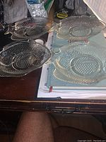 Four clear glass fish-shaped snack plates with a raised circle cup holder in the center shown from above on a desk surface.