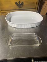 White Corning Ware casserole dish and clear glass lidded butter dish sitting on stainless steel surface