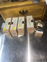 Photo of 18 boxed sets of Amazon Basics Dual Tip Calligraphy Brush Pens and one box containing three neck lanyards on a metal surface.