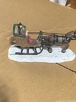 Side view of the horse and sleigh figurine showing two passengers in Victorian attire on a white snow-like base
