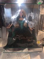 Front view of the 2004 Holiday Barbie doll in its original packaging. The doll wears a green velvet dress with sparkle details, visible through the clear plastic window. Snowflake decorations and silver-edged box are also seen.