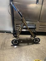 Side view of knee walker with four wheels, padded knee rest, and metal frame.
