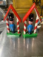 Two vintage wooden nutcracker ornaments under red roofs with candy cane pillars, standing on green bases.