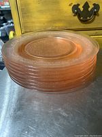 Stack of eight pink glass salad plates showing thickness and edges with floral pattern visible in translucent pink glass.