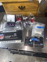Lot contents on metal surface showing all items grouped including license plate frame, cleats in packaging, eye protection glasses, guitar parts and electric meter.