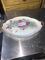 Oval porcelain serving plate on metal surface, showing overall shape and gold edging
