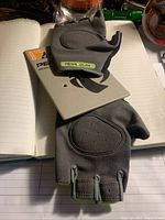 Pair of gray padded fingerless cycling gloves with ventilation holes on palm side, resting on a notebook surface with attached tags.