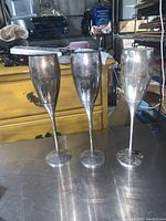Three silver plated champagne flutes standing upright, showing tarnish and need for cleaning.