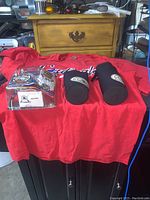 Red vintage St. Louis Cardinals T-shirt with two black Daytona Bike Week drink cozies and a small box on top, items arranged on table with drawer background.