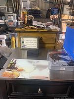 Lot contents showing corkscrew, decorative wine sign, cutting board and wine stoppers on a table with background storage items.