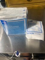 Photo showing the sealed box of Medline woven gauze sponges and the sealed roll of gauze bandage on a metal surface.
