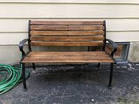 Front view of wooden and wrought iron bench with wooden slats and black frame.