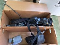 Box containing multiple cameras including a Panasonic Omni movie camera with shoulder strap and a Nikon Coolpix camera.